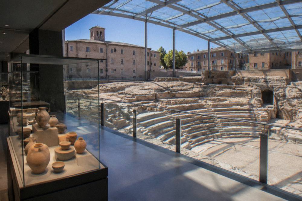 Interior gallery of the museum with display cases of Roman ceramics beside a view of the ancient theatre walls