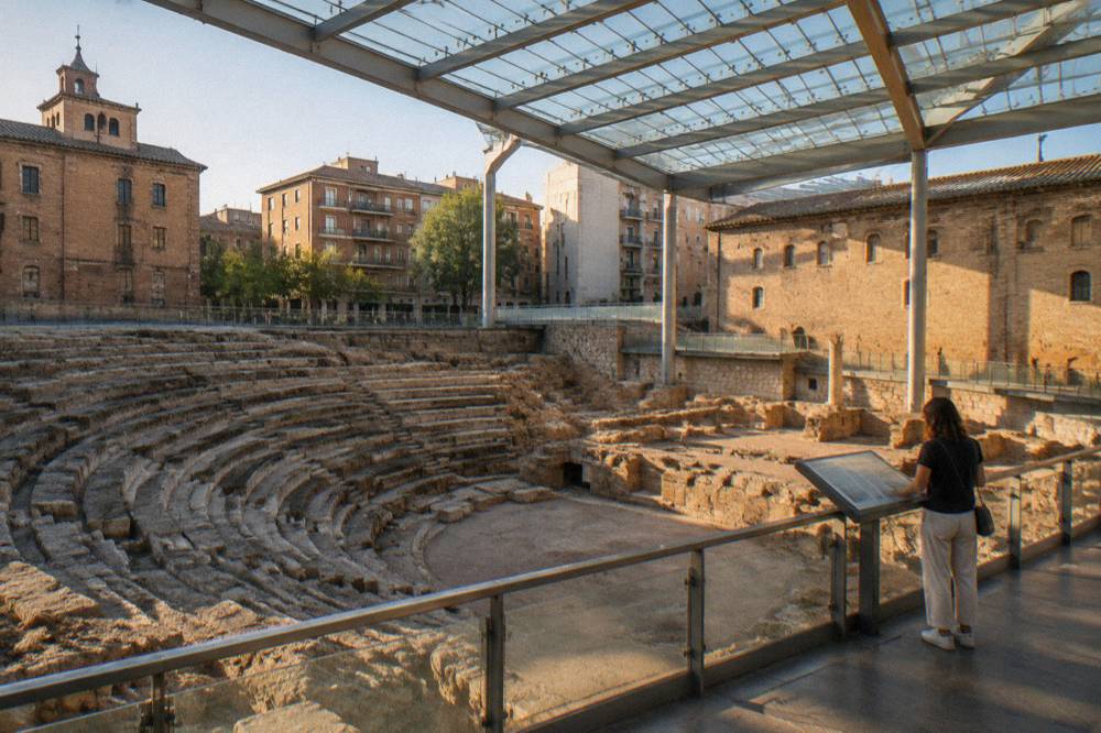 A museum visitor reading an information panel above the exposed Roman masonry of the theatre stage area