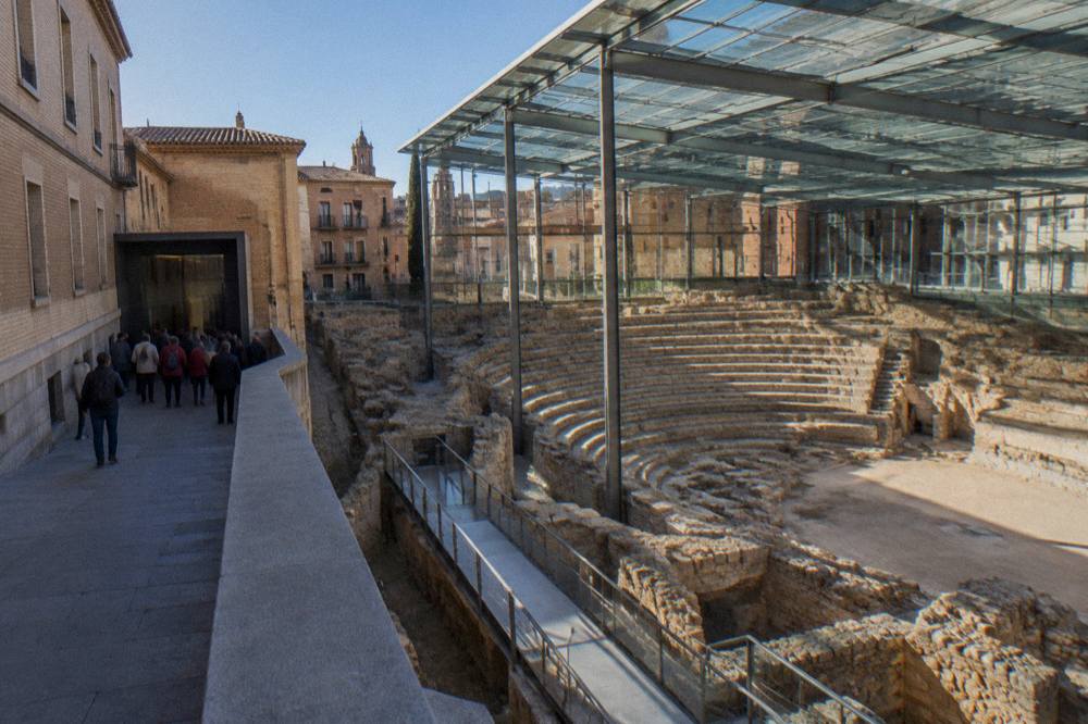 Visitors on a guided walk pausing at the entrance of the Roman Theatre Museum in a narrow Zaragoza street