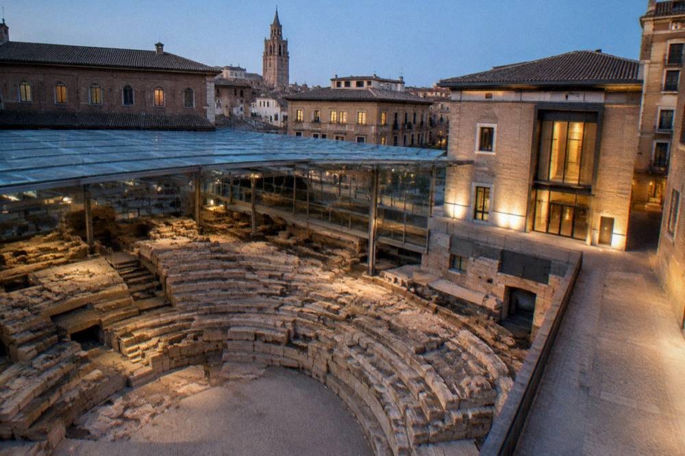 The evening facade of the Roman Theatre Museum entrance lit softly on a quiet street in old Zaragoza