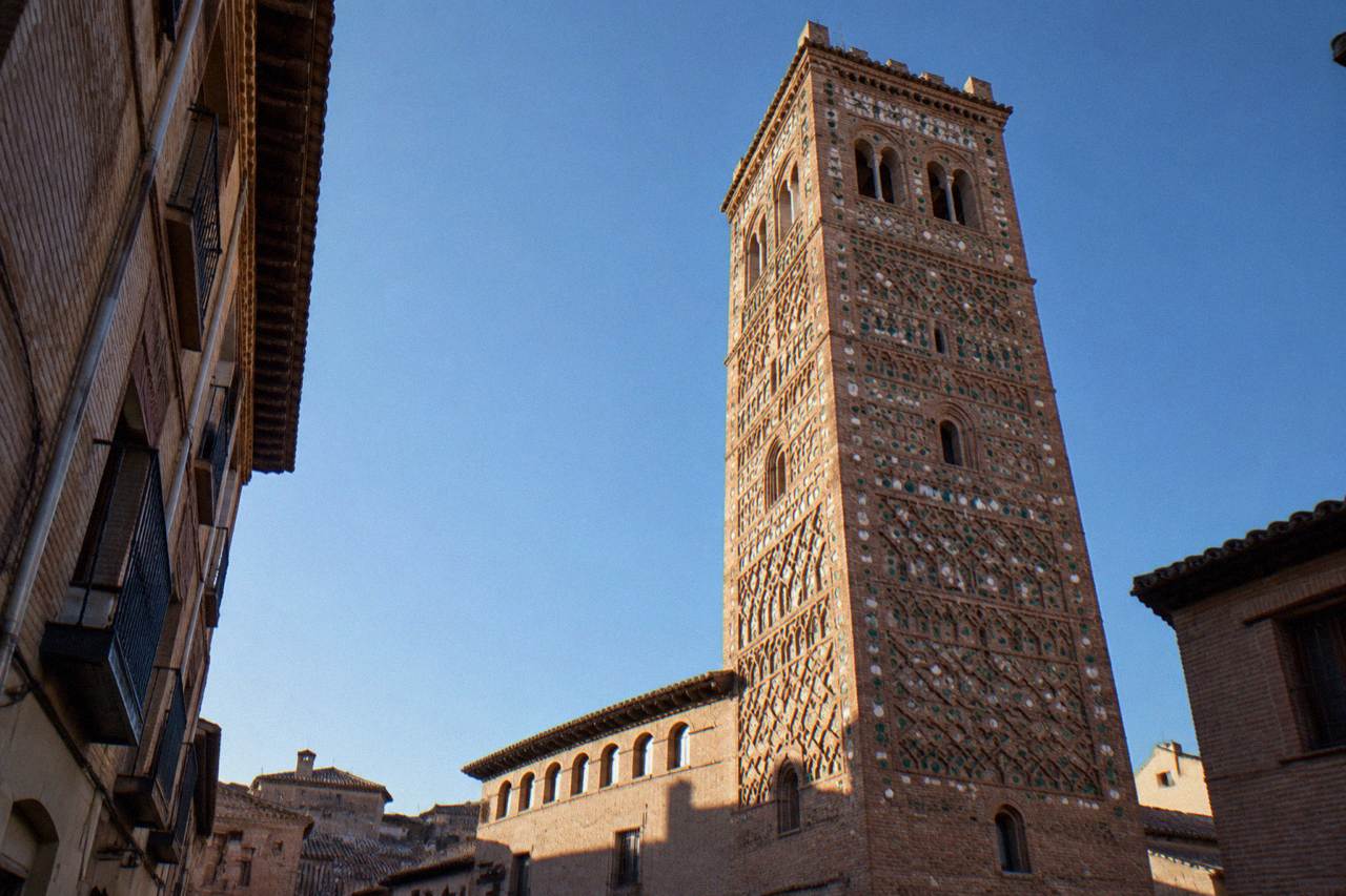 A quiet old town street in Zaragoza with brick Mudejar style buildings under a clear blue sky