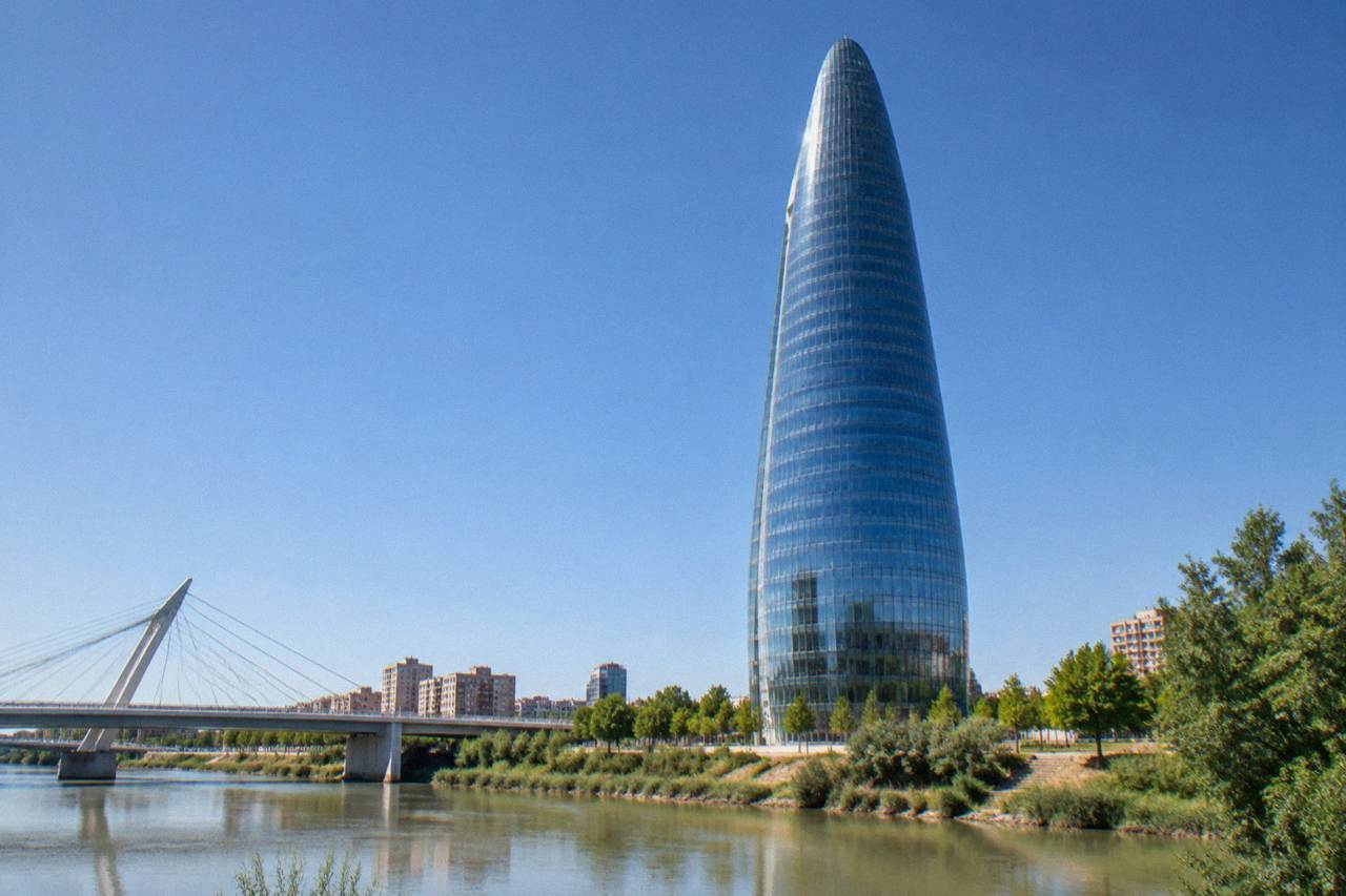 A tall water tower building rising above the Ebro river meadow in Zaragoza under a clear sky