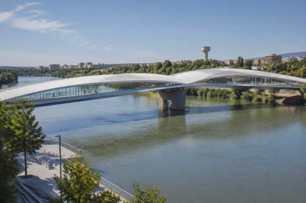 A white covered bridge pavilion spanning the Ebro river with the water tower visible beyond it