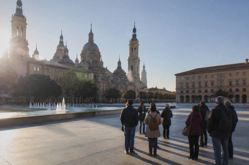 A guided walking group listening to a guide in a stone square in Zaragoza's old town