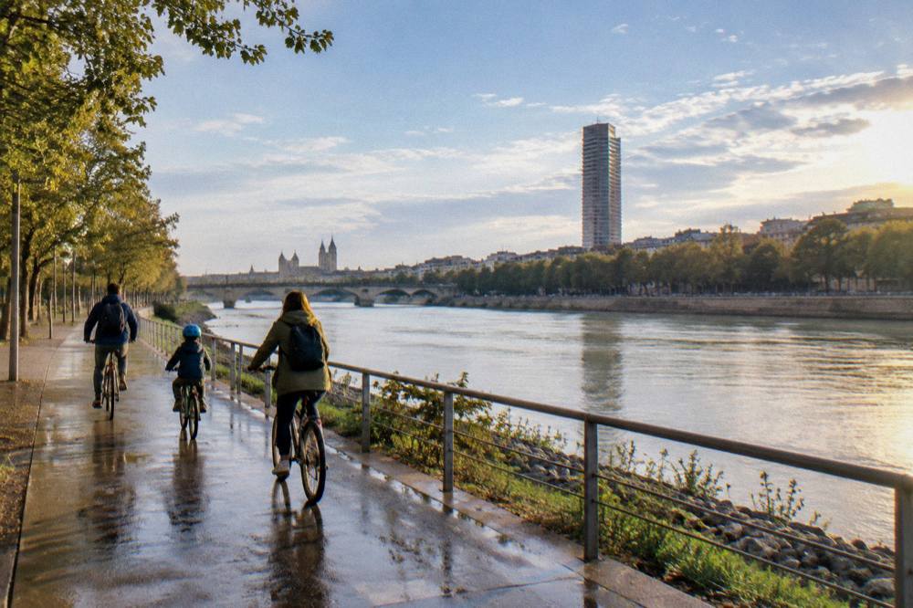 A family cycling along a riverside path beside the Ebro with a modern tower building ahead