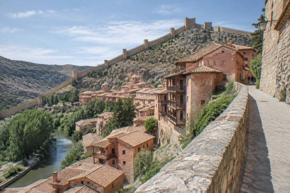 Medieval stone wall walkway following a hillside above red rooftops