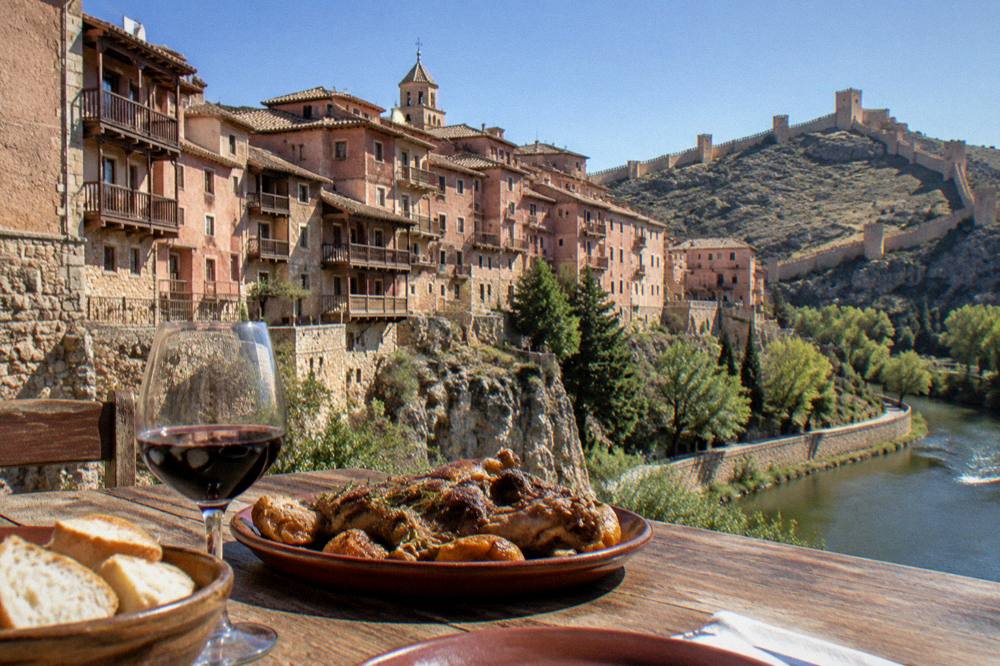 Wooden dining table with roasted lamb, red wine and rustic bread