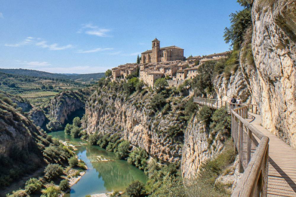 A wooden walkway fixed to a limestone cliff above a green river with pools below