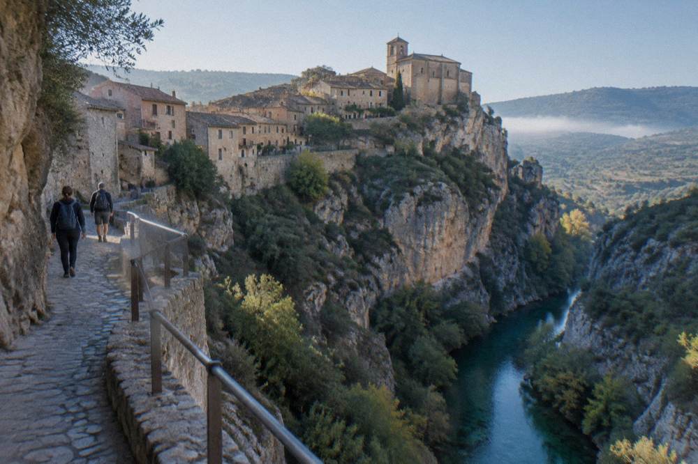 Walkers on a cliff-side walkway looking down into a narrow canyon with clear water below