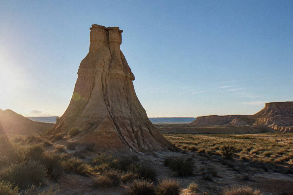 Close view of a tall eroded clay formation standing alone on a flat scrub plain