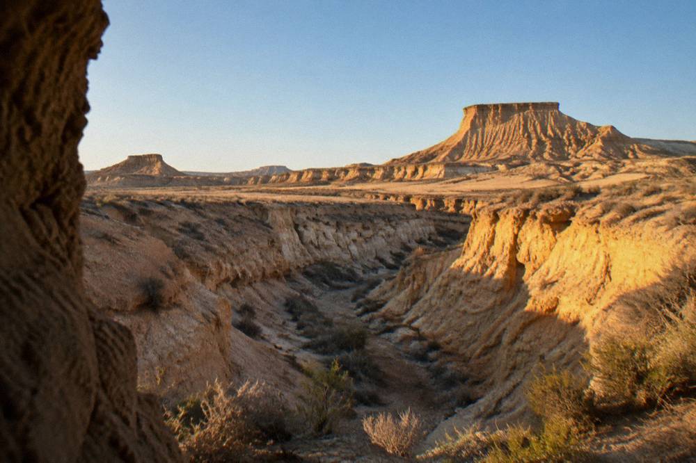 Dry ravine with steep eroded clay walls and sparse low scrub under a clear sky