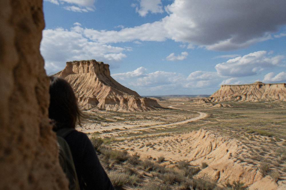 Pale ochre badland hills with a winding dirt track crossing the plain toward the horizon