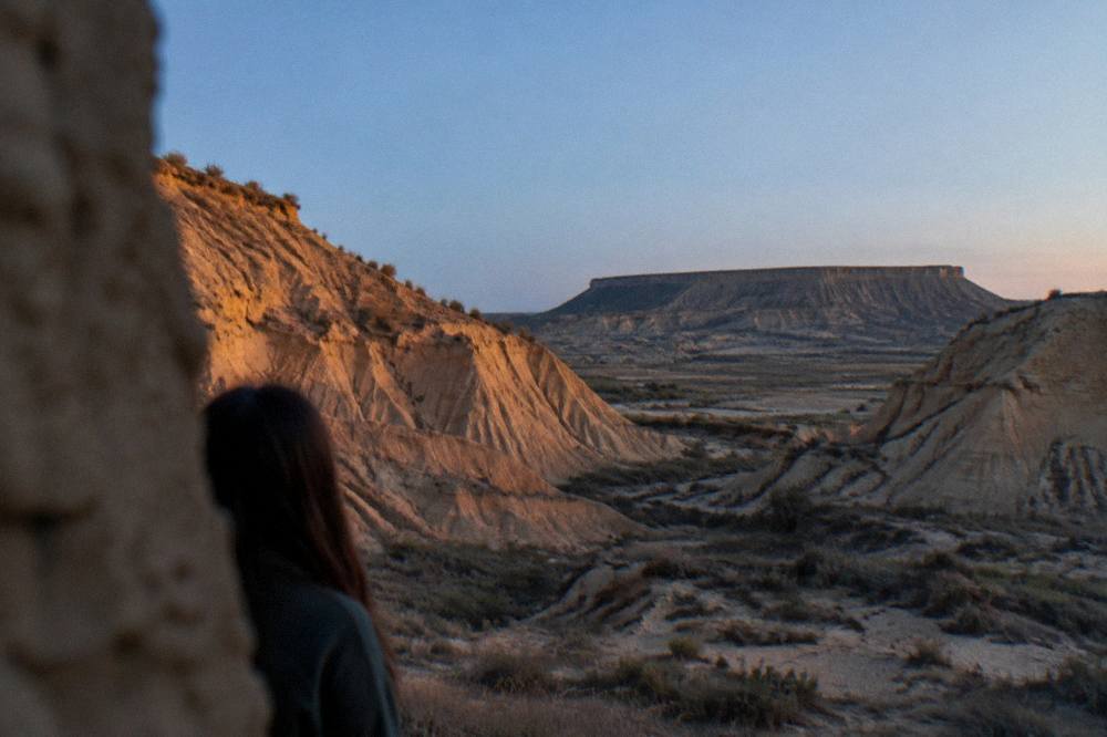 Evening view of a dry badland valley with soft golden light on eroded slopes and a distant plateau