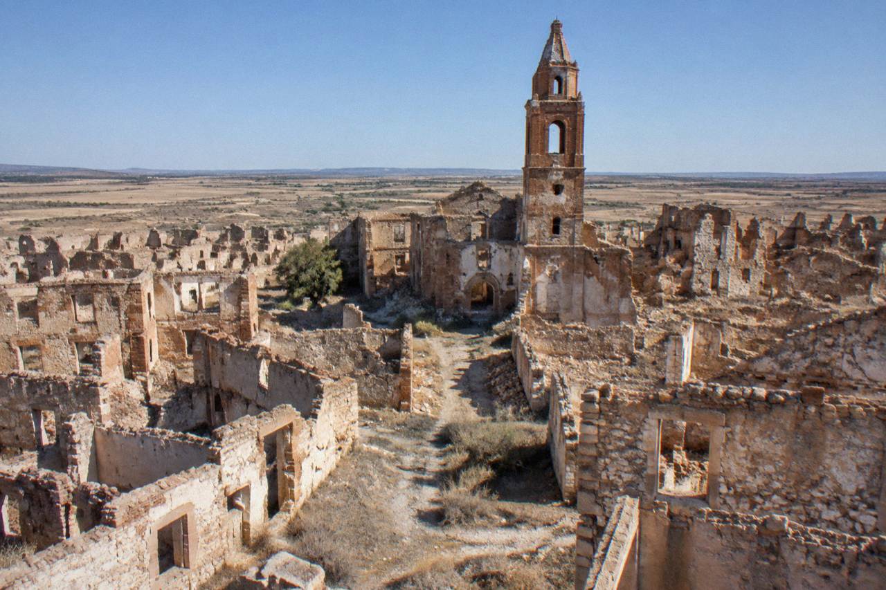 Ruined stone houses and a broken church tower under a wide dry sky at Belchite old town