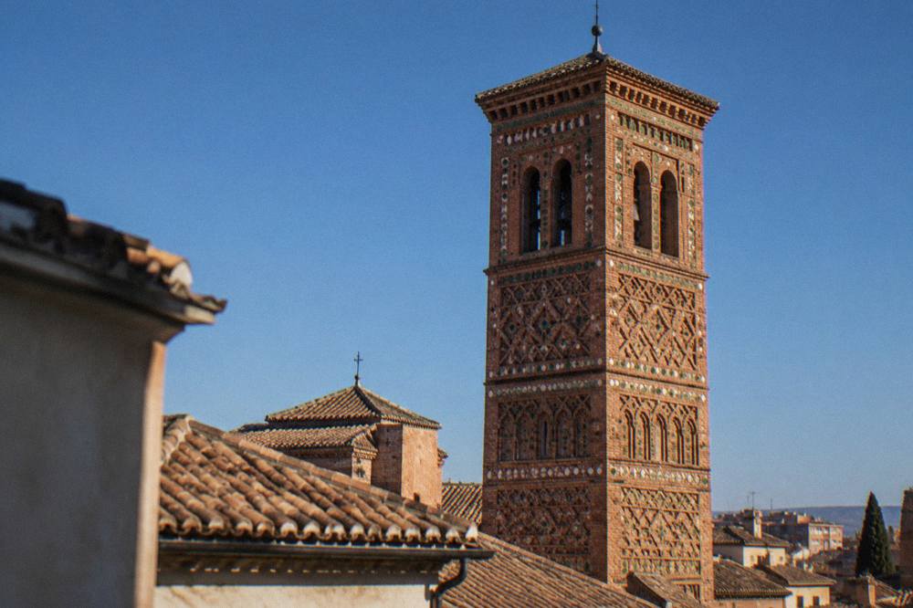 A brick Mudéjar church tower with geometric patterning rising over tiled roofs