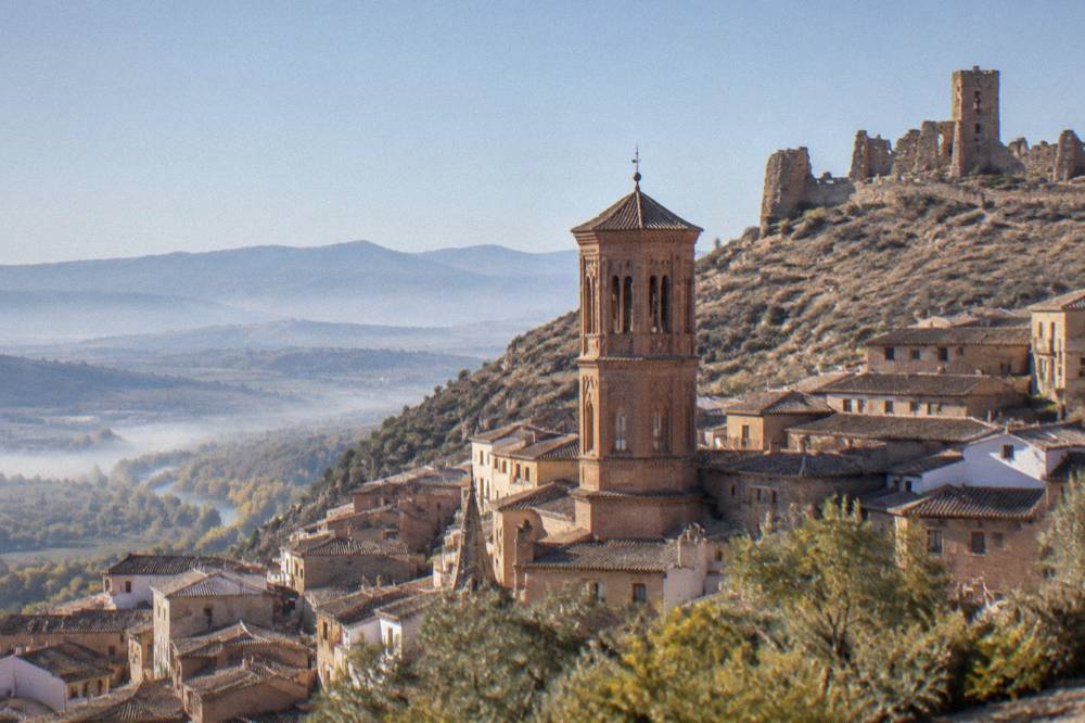 Stone ruins of a hilltop castle wall above a Spanish town with the valley beyond