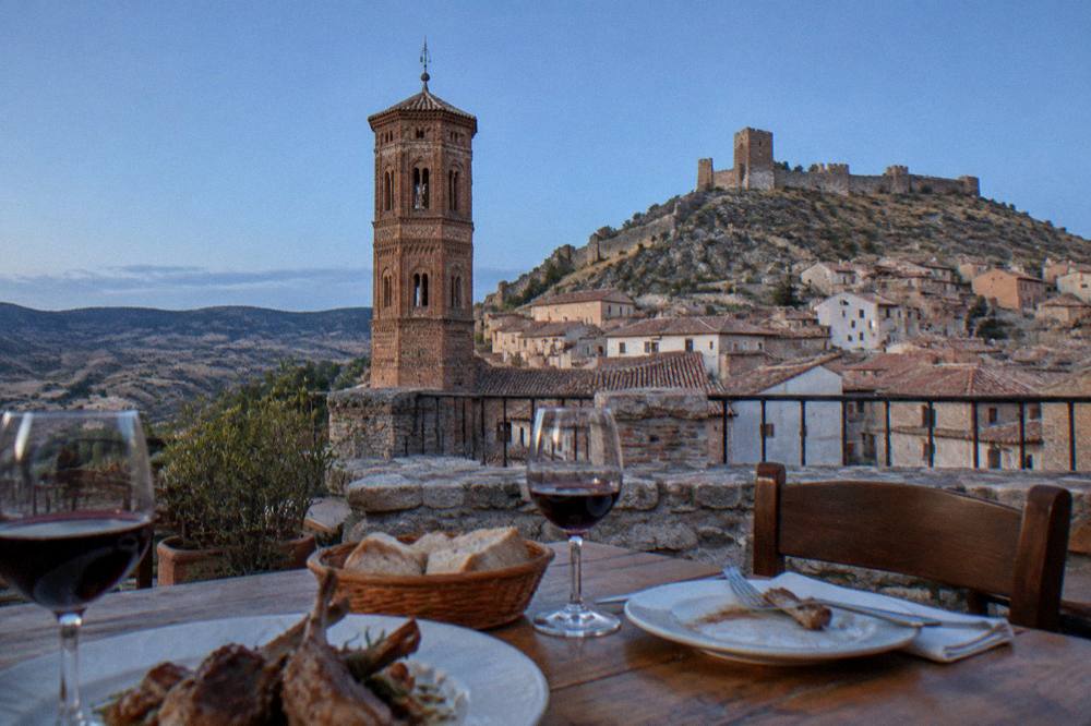 A rustic restaurant table with red wine glasses and plates of lamb and bread