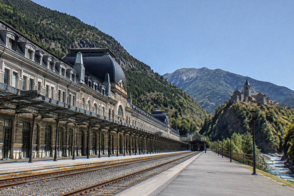 A hilltop stone village with a church tower overlooking a river gorge and forested mountains
