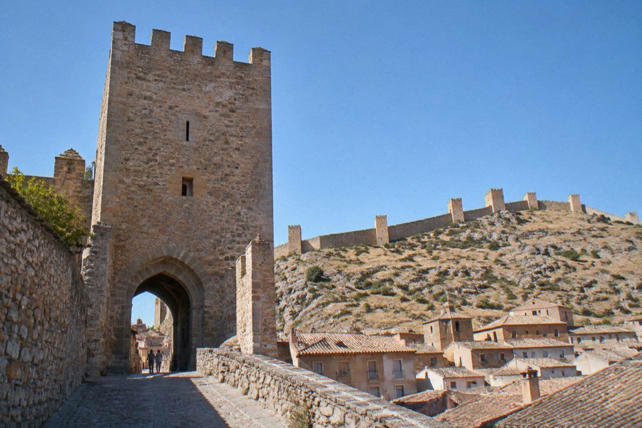 A stone gateway tower in a medieval Spanish walled town with hills behind it under a clear sky
