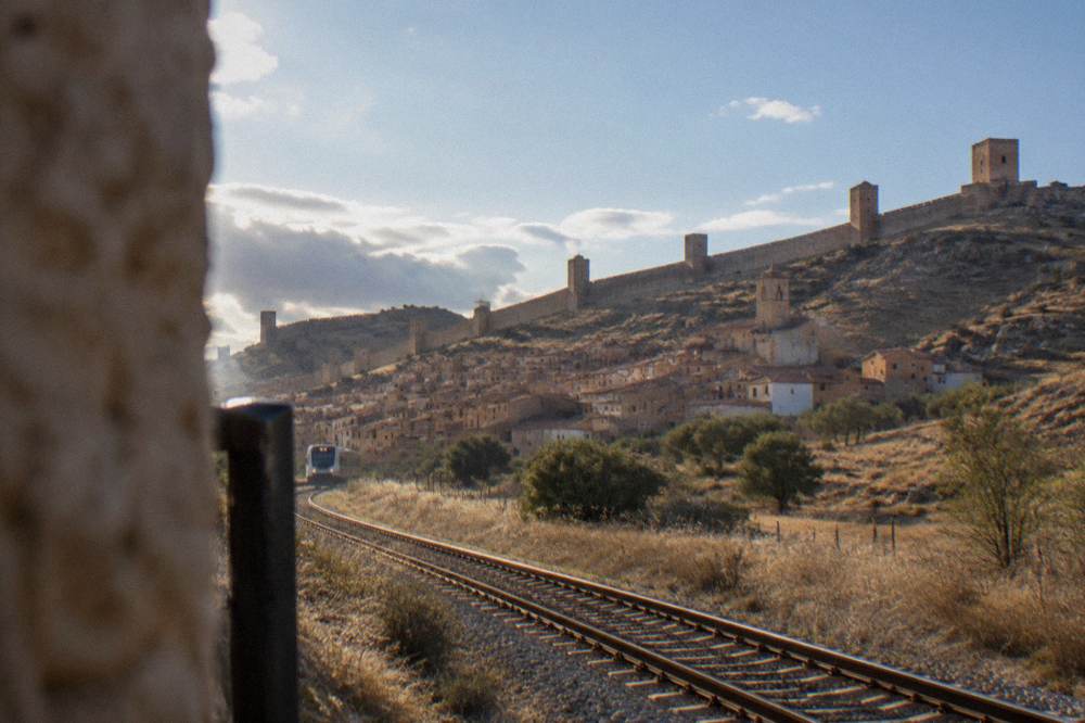 A single-track railway line running through dry plateau country towards a Spanish hill town