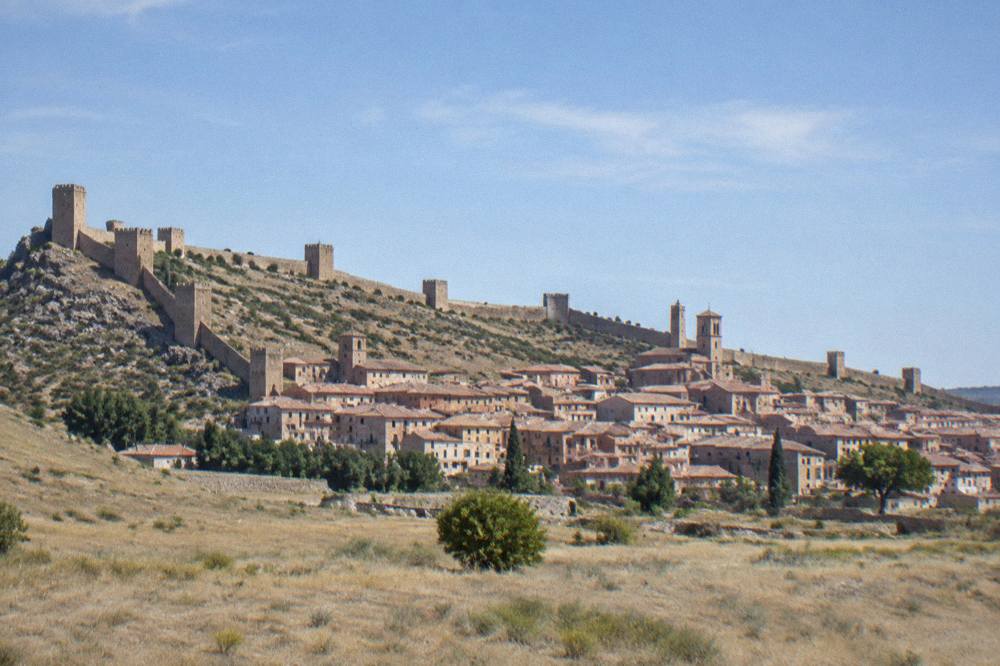 A wide view of a walled Spanish hill town from across dry open plateau country
