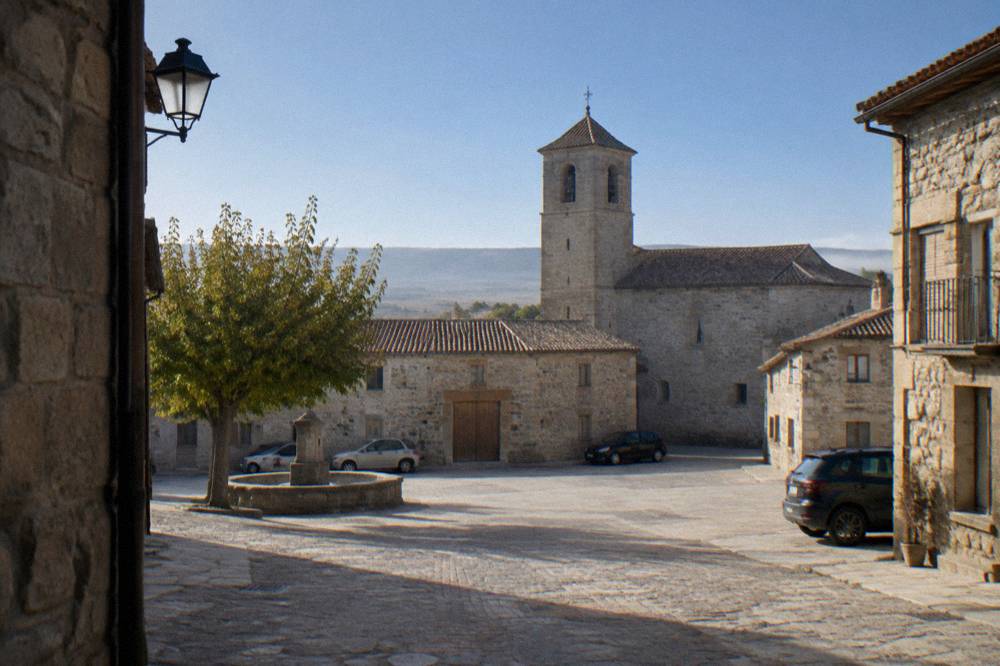 A quiet village square with stone buildings and a few parked cars in afternoon light