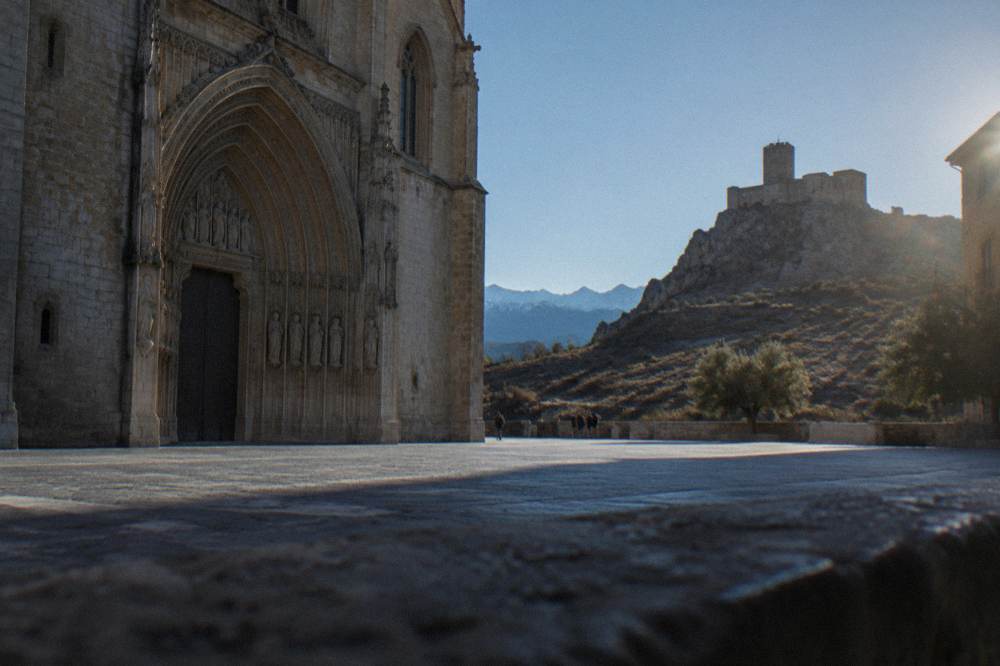 A Romanesque castle keep standing on a rocky ridge above dry sierra foothills