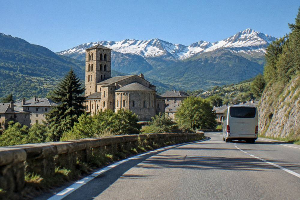 A coach winding along a road between green mountain slopes in the Pyrenees