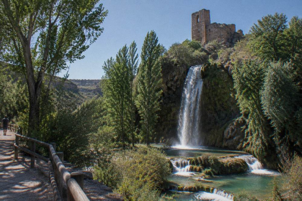 A tall waterfall falling over dark rock into a pool surrounded by trees