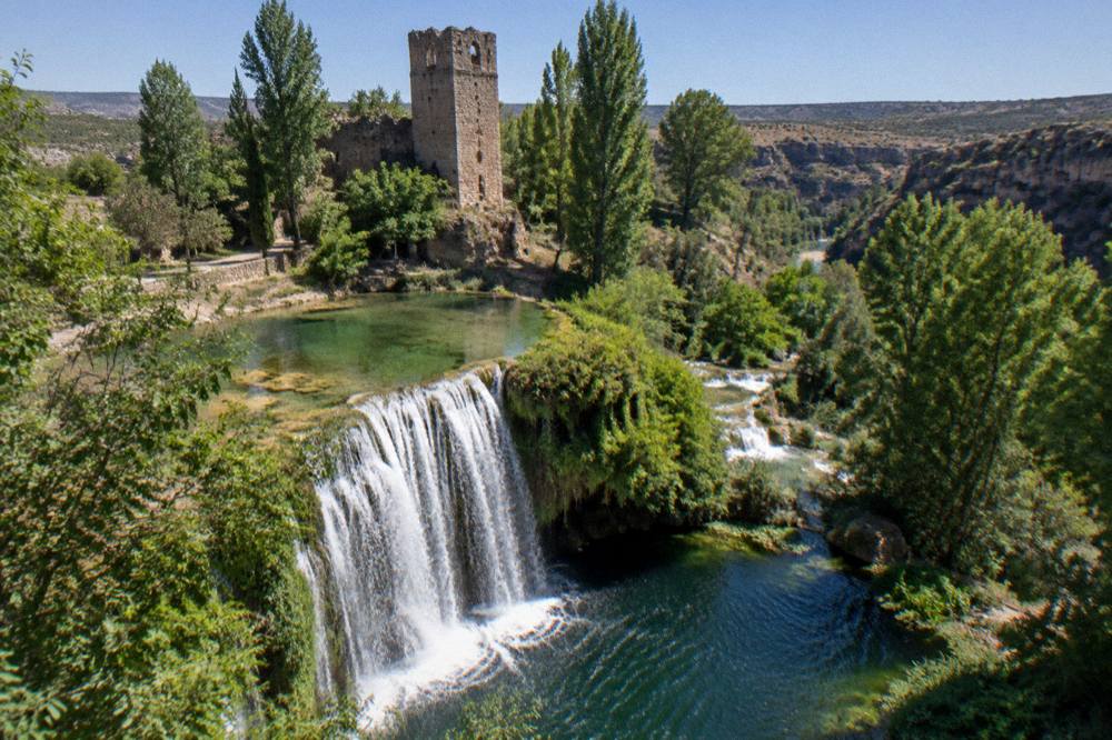 Water falling over a curved stone lip into a dark pool with green plants at the edges