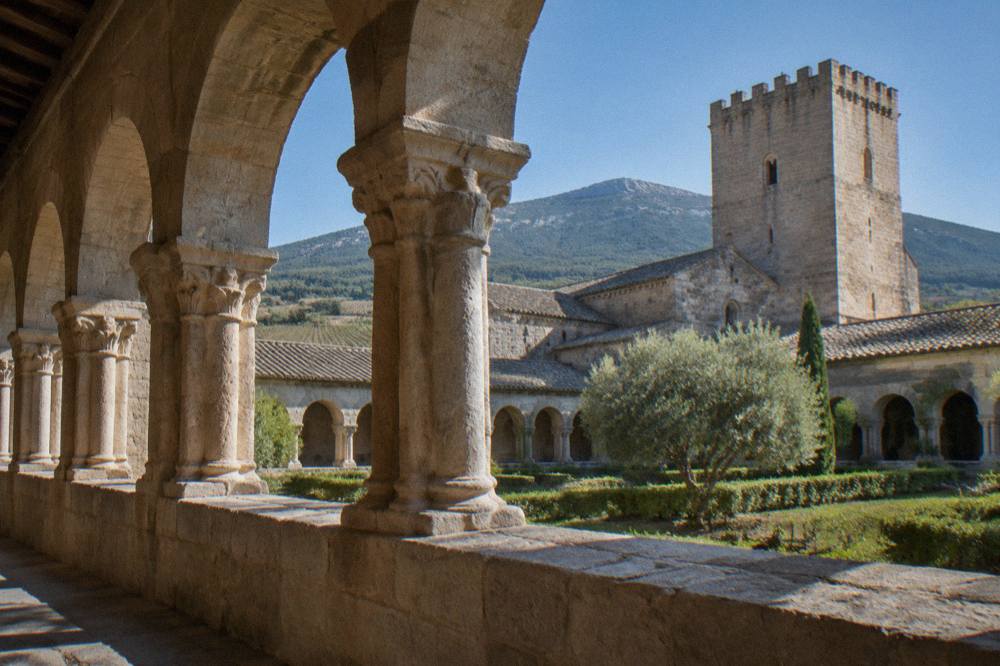 Interior of a stone monastic cloister with arched walkways and worn columns