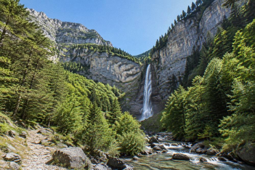 A tall waterfall falling in a narrow rocky gorge surrounded by green forest