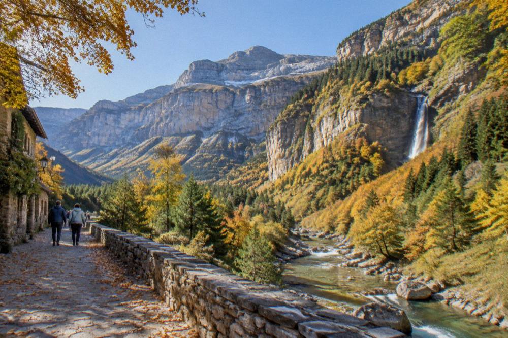 A wide view of a glacial valley with layered rock cliffs and autumn coloured forest below