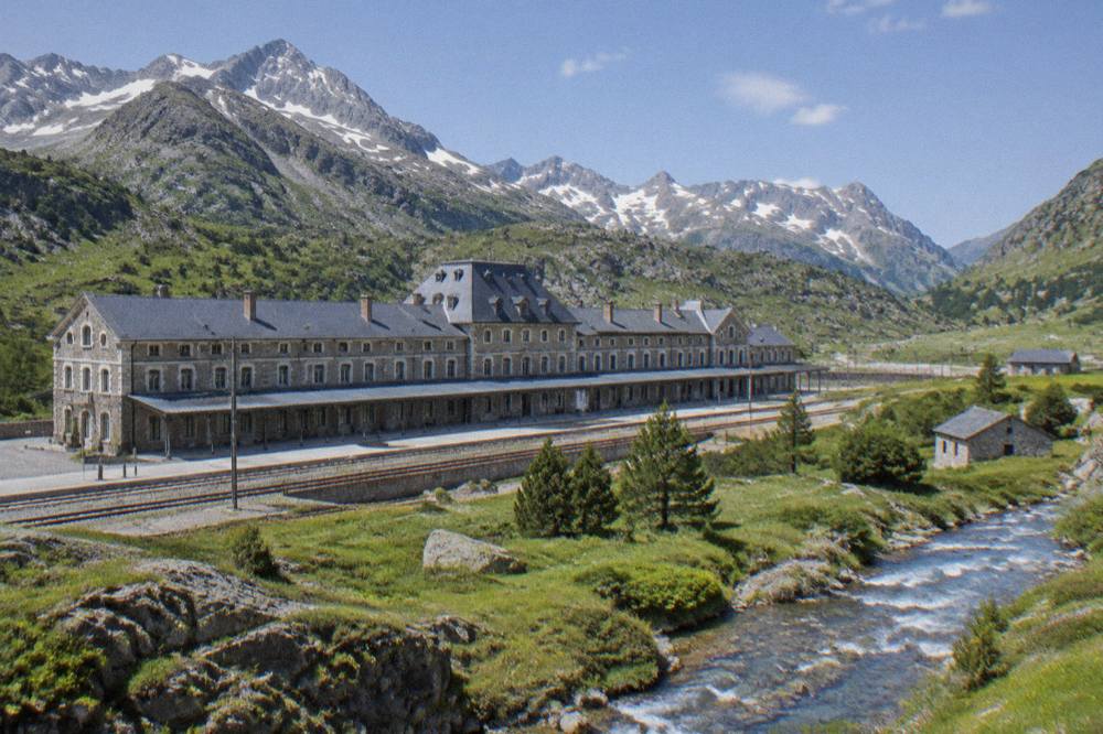 Large old railway station building with a long stone façade and a mountain ridge behind it