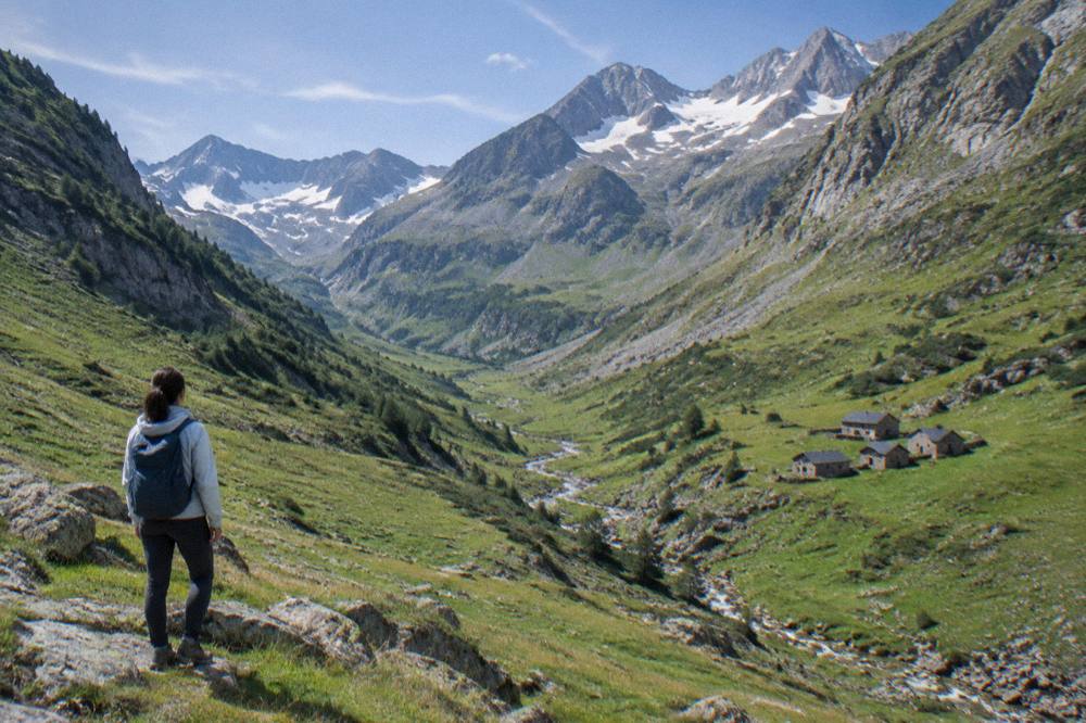 Hiker in a light jacket looking out over a green glacial valley with steep walls