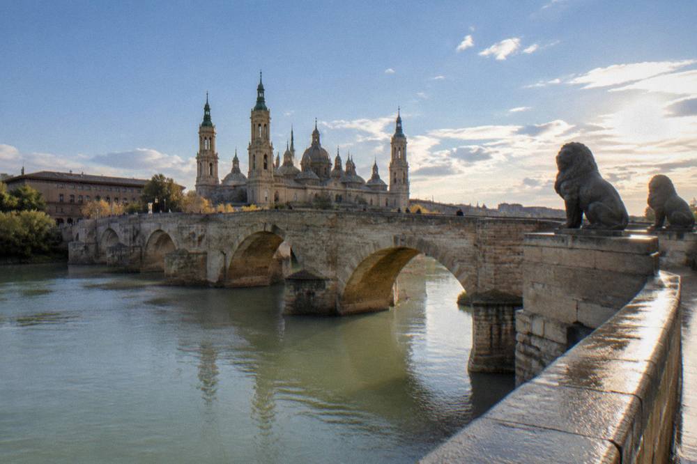 Stone bridge over a clear river with mountains rising behind a small town