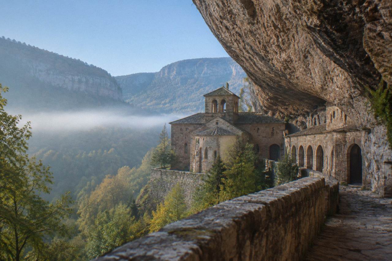 The old monastery of San Juan de la Peña built into the base of a large rock overhang in a wooded Pyrenees valley