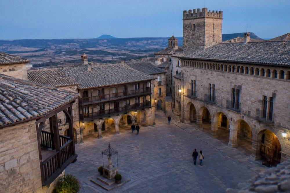 An arcaded stone square with wooden galleries and a palace facade in a hill town