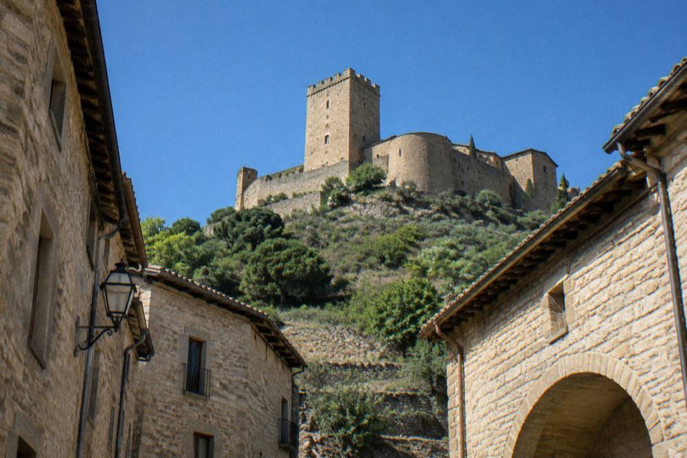 A Romanesque stone castle on a hilltop above green foothills in Aragon