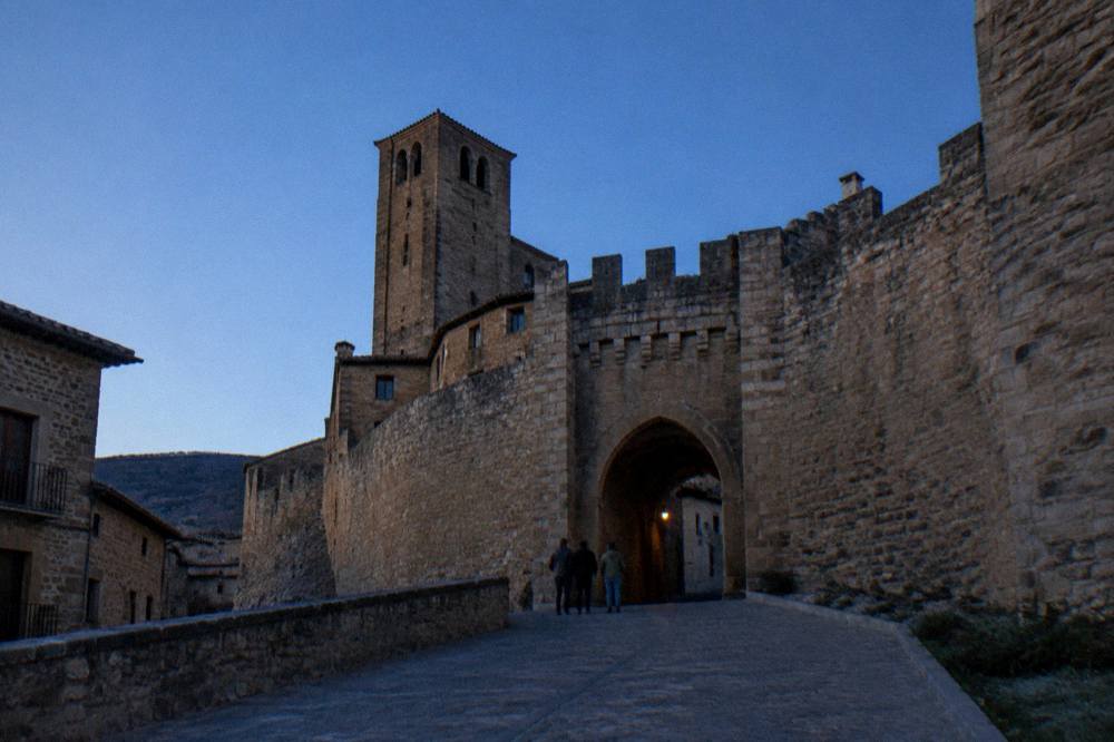 A stone gateway in a medieval town wall with hills behind it under a blue sky