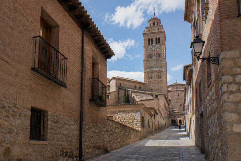A narrow stone street climbing between old brick buildings toward a bell tower