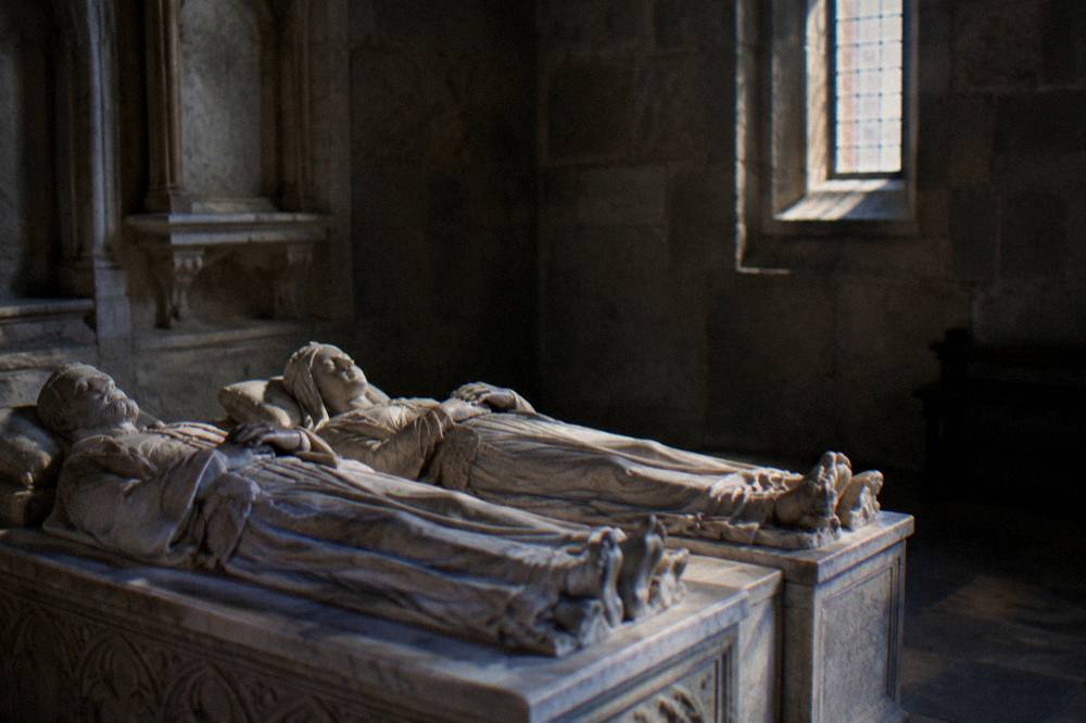 Two carved stone figures lying side by side on marble tombs inside a dim chapel