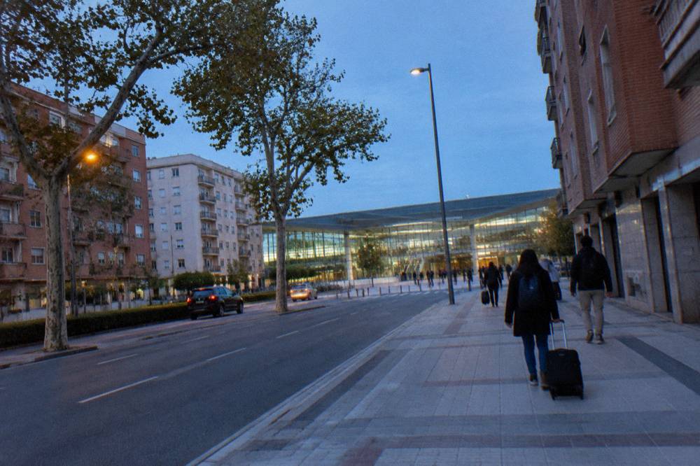 A modern station hall with tall glass walls and travellers moving toward the exits