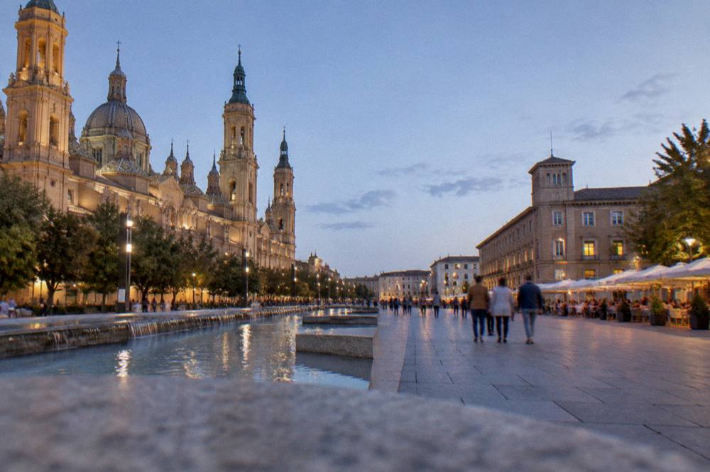 An evening street in a Spanish old town with lit restaurant terraces and people walking