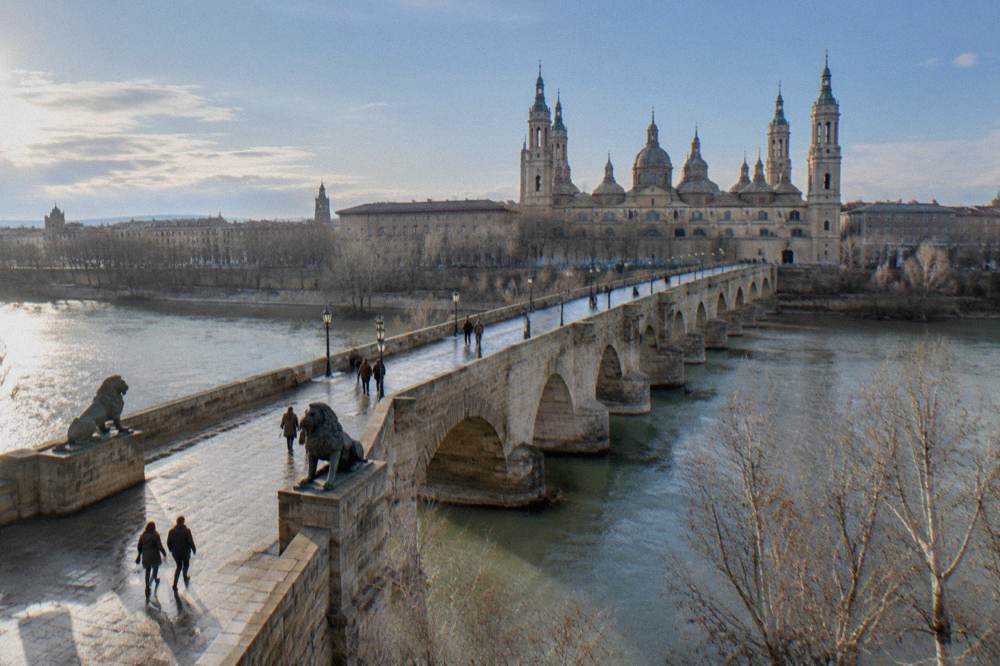 The stone bridge and the river Ebro under a pale winter sky with bare trees along the bank