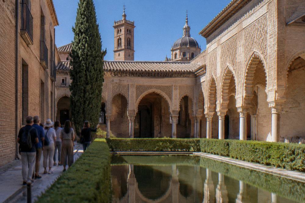 A guided group standing in a Moorish courtyard with carved plaster arches and a reflecting pool