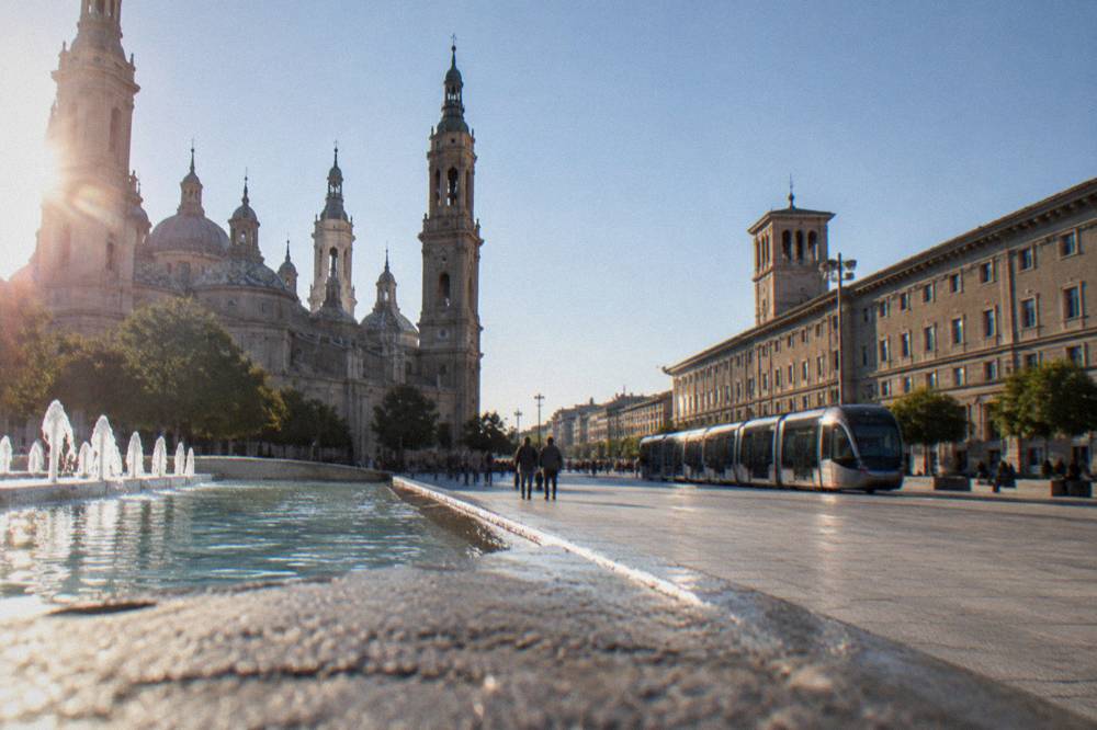 A tram passing through a sunny Zaragoza street with stone buildings on both sides
