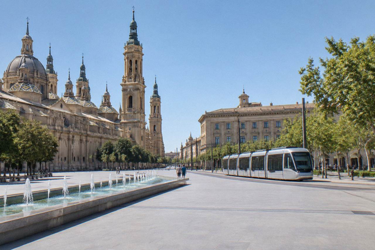 A modern tram travelling along a tree-lined avenue in Zaragoza with historic stone buildings behind it