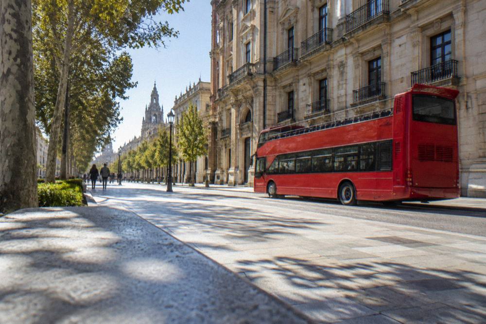 A red open-top sightseeing bus parked on a city street beside a historic palace facade
