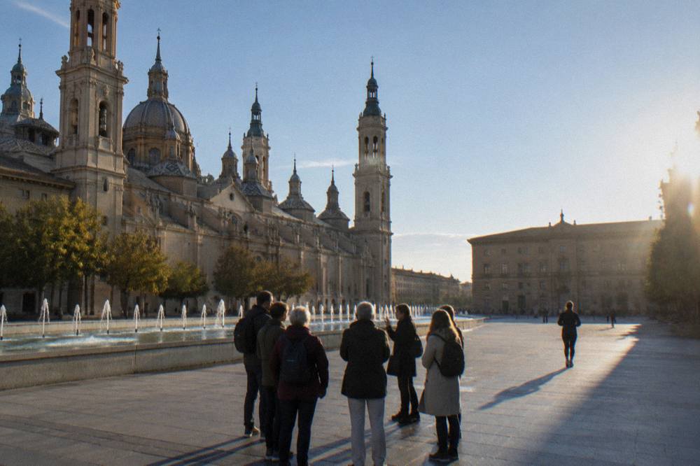 A small guided group standing with a guide outside a gothic cathedral entrance in Zaragoza